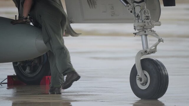 Technician kneeling beneath fighter jet fuselage near landing gear conducting technical inspection before flight