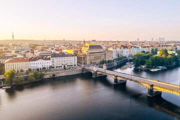 Obraz premium The National Theatre stands prominently along the Vltava River in Prague, capturing the golden tones of sunset.