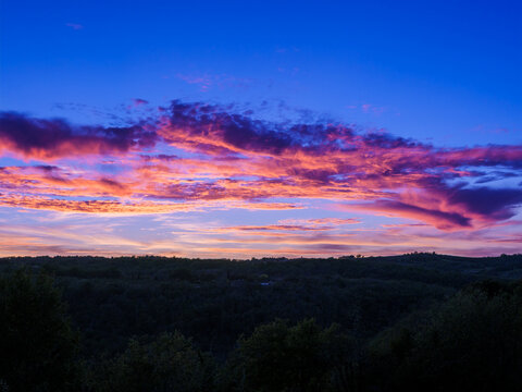 eep Blue Sunset Sky with Vibrant Orange and Magenta Clouds Over Forest