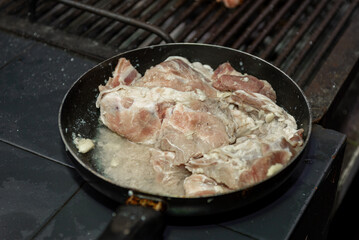 A close-up shot of raw pork being cooked in a frying pan on a stovetop