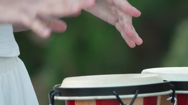 Drumming, hands, rhythm, close-up of a person playing bongo drums outdoors.