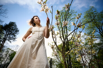 Smiling woman portrait outdoors near blooming magnolia flowers in spring garden. Natural beauty, fresh skin, and joyful expression in soft sunlight. Concept of spring and harmony with nature