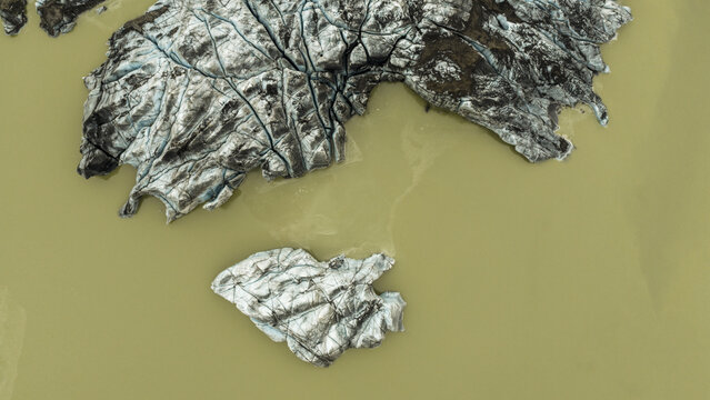 Aerial view of glacial ice drifts in the lagoon, their jagged forms contrasting sharply with the murky water, Solheimajokull, Myrdalshreppur, Iceland.