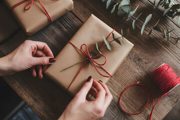 Hands wrapping gift with brown paper and red twine on wooden table gift wrapping