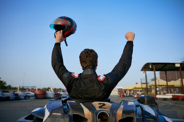 A go-kart racer raises their helmet in triumph after winning a race