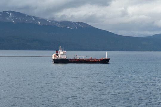 Aerial view of a tanker ship cutting through the tranquil, deep blue waters, against a backdrop of rugged mountains under a cloudy sky, Puerto Williams, Chile.