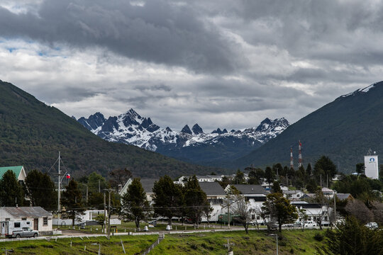 Aerial view of the town nestled between green hills and snow-capped Dientes de Navarino mountains under a dramatic sky, Puerto Williams, Chile.