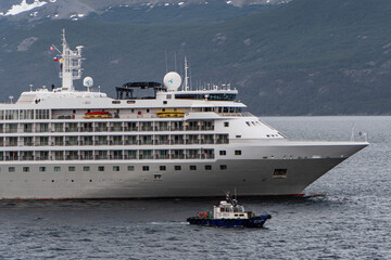 Aerial view of a cruise ship sailing near a small boat, the dark waters contrasting with the ship's white exterior, Puerto Williams, Chile.