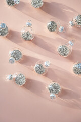 Clear Christmas ornament with silver glitter detail on pink background.