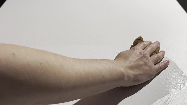 Close-up view of a white kitchen table surface being wiped by a hand with a sponge and cleaning