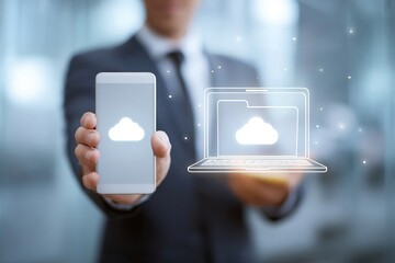 Smartphone displaying folder icon in hand, with laptop featuring cloud symbol on wooden desk, illustrating digital storage and technology concepts in modern workspace