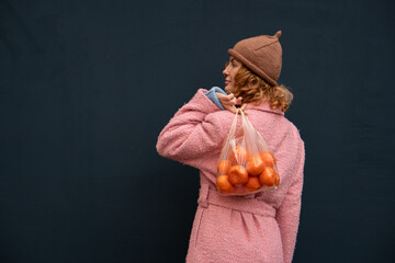 Woman in a pink coat with tangerines over her shoulder on a dark background