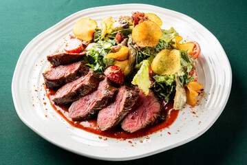 A vibrant, gourmet steak salad is served on a white plate, showcasing perfectly seared, sliced rare beef and a fresh mix of greens, cherry tomatoes, and crispy potato chips