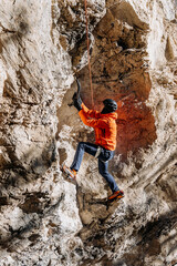 Male Dry Tooling Climber In Red Jacket On Steep Rock Face: Technical Ascent Using Ice Axes, Crampons, And Rope On Vertical Limestone Cliff