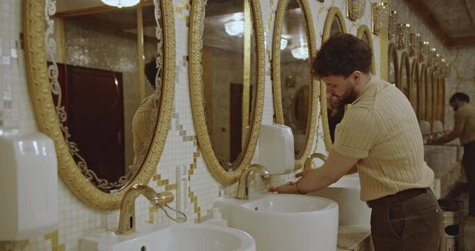 Businessman washing and drying his hands in a modern and elegant washroom. The restroom features stylish mirrors and a luxurious atmosphere.