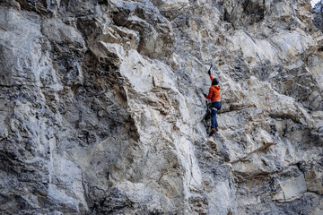 Male Dry Tooling Climber In Red Jacket On Steep Rock Face: Technical Ascent Using Ice Axes, Crampons, And Rope On Vertical Limestone Cliff