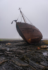 An old fishing schooner is stuck on the rocky Barents Sea, Rybachy Peninsula. The vessel is covered in rust