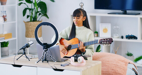 Girl, guitar teacher and influencer with laptop, home and recording video for content creation on web. Teenager, computer and ring light with instrument, podcast and music tutorial on social network