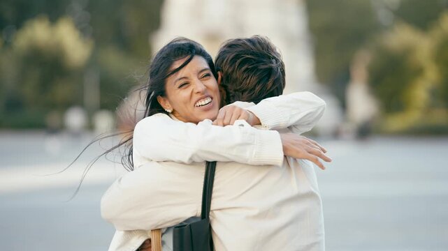 Joyful woman with long dark hair running with open arms to meet her partner. Emotional reunion of a loving couple embracing in a city square