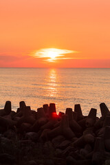 An orange sunset over the sea, the sun low on the horizon. A coastal landscape visible from the shore between the rocks.
