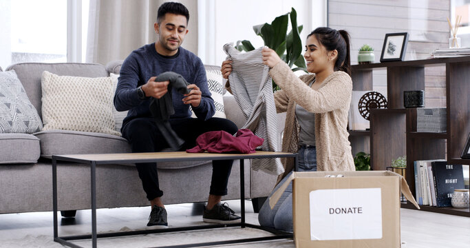 Couple, fold clothes and donation box in living room for charity, nonprofit support or declutter home. Married people, apparel giveaway or parcel in house for NGO initiative, help or spring cleaning.