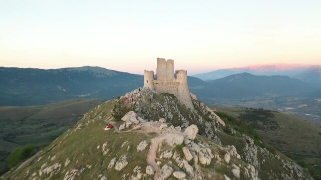Aerial view of Rocca Calascio, a medieval fortress perched atop a rocky outcrop, with people scattered around the landscape, Calascio, Abruzzo, Italy.