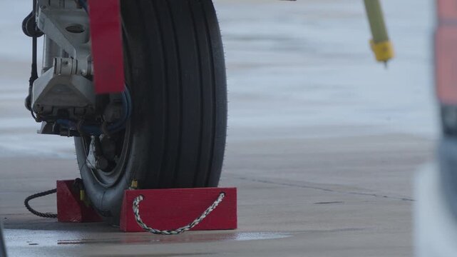 Close view of fighter jet landing gear wheel locked with chocks on wet runway surface during ground safety procedure