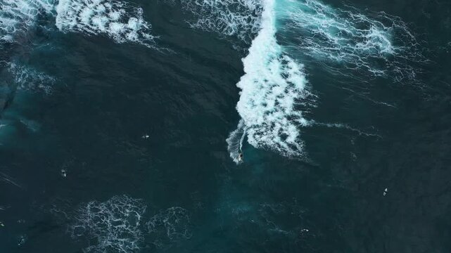 Aerial view of a surfer riding a wave as waves crash along the dark coast, creating a stunning visual contrast, Benijo, Santa Cruz de Tenerife, Spain.