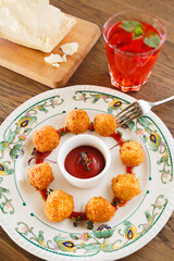 Crispy golden cheese croquettes arranged on a floral plate with tomato sauce, paired with a refreshing berry drink