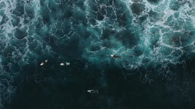 Aerial view of surfers bobbing in the dark, frothy ocean water, the white foam contrasting against the deep blue, Benijo, Santa Cruz de Tenerife, Spain.