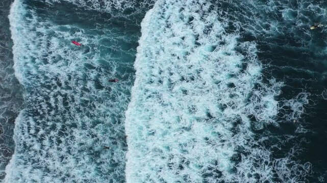 Aerial view of surfers riding the vibrant, foamy waves of the ocean, creating a stunning contrast against the deep blue sea, Benijo, Santa Cruz de Tenerife, Spain.