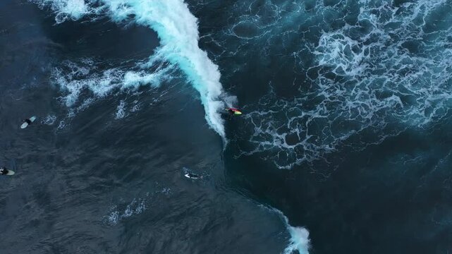 Aerial view of surfer riding the crest of an enormous wave, while others wait in the dark blue ocean waters, Benijo, Santa Cruz de Tenerife, Spain.