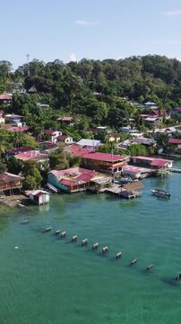 Vertical aerial establishing shot showcasing a picturesque stilt house village surrounded by turquoise water on Bastimentos Island, Panama.