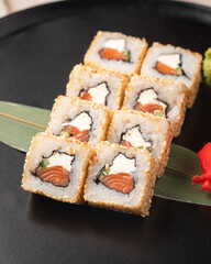 Sesame coated sushi rolls with fresh salmon and cream cheese served on a black plate with ginger