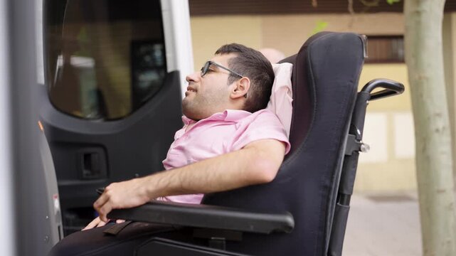 Man with a disability sitting in his wheelchair being lowered by an accessible van's lift. An assistant helps him during the transfer