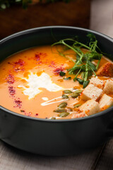 Creamy pumpkin soup topped with fresh herbs seeds and crunchy croutons served in a dark bowl on rustic table
