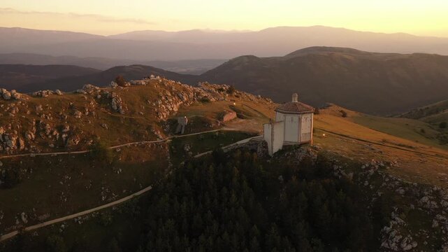 Aerial view of the octagonal Santa Maria della Pieta standing proudly on the ridge, bathed in the warm glow of sunset, Calascio, Abruzzo, Italy.