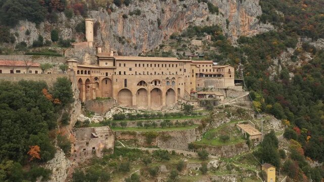Aerial view of St. Benedict's Abbey nestled in the mountains, with its weathered stone walls contrasting against the vibrant greenery, Subiaco, Lazio, Italy.