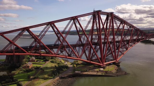 Aerial view of the iconic red Forth Bridge spans across the water, a cruise ship sailing in the background under a partly cloudy sky, Inverkeithing, Scotland, United Kingdom.