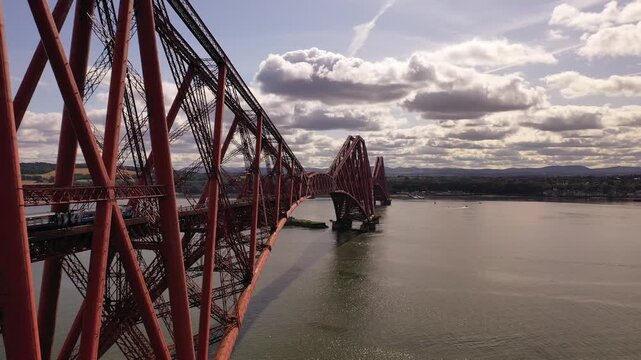 Aerial view of the red steel Forth Bridge spanning across the calm waters under a cloudy sky, a marvel of engineering, Inverkeithing, Scotland, United Kingdom.