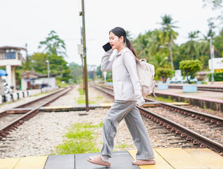 Asian woman using phone call and walking at train station. Tourist female with luggage, smartphone walk in holiday background concept. Travel Thailand. Person suitcase 