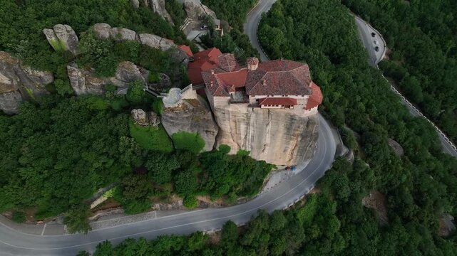 Aerial view of the Monastery of Rousanou perched atop a stunning rock formation, surrounded by lush green trees, Meteora, Greece.