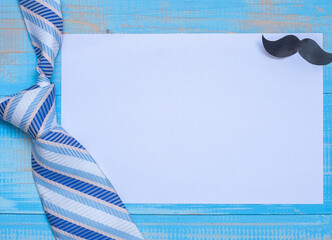 Blank paper with striped necktie and mustache icon on blue wooden background, Father’s Day, business greeting, promotion, or branding concept