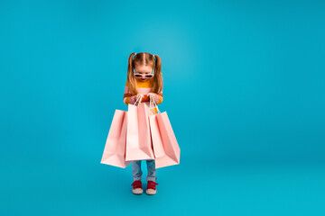 Young girl with pink shopping bags smiles against blue background wearing jeans and sunglass