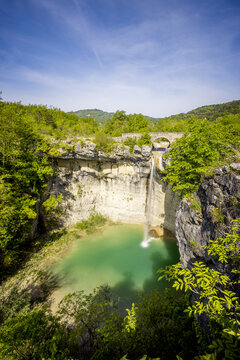 View of a stunning waterfall cascading into a vibrant turquoise pool surrounded by lush green trees under a clear blue sky, Kotli, Istria County, Croatia.