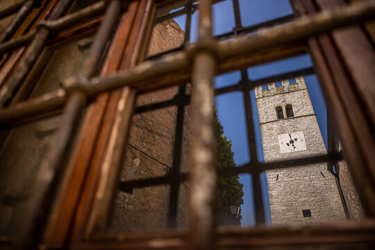 View of a weathered window frame offering a glimpse of a stone clock tower under a bright blue sky, evoking a sense of timelessness, Buzet, Istria County, Croatia.