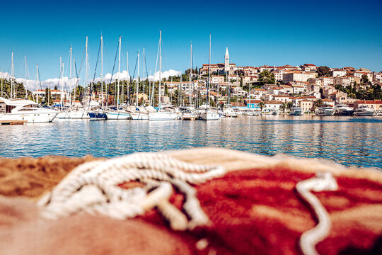 View of sun-kissed boats bobbing gently in the azure harbor, a historic town perched atop the hill, framed by a textured fishing net, Vrsar, Istria County, Croatia.