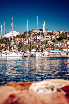 View of boats bobbing gently in the azure harbor beneath a sun-drenched, terracotta-roofed town crowned with a striking white church tower, Vrsar, Istria County, Croatia.