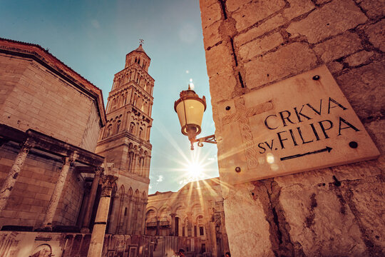 View of the radiant sun illuminating the ancient stone walls and towering bell tower, casting long shadows on the cobblestone street, Split, Split-Dalmatia County, Croatia.