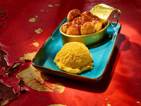 EIskugel Mango mit Tiramisu in Blechdose auf blauer Steingutplatte